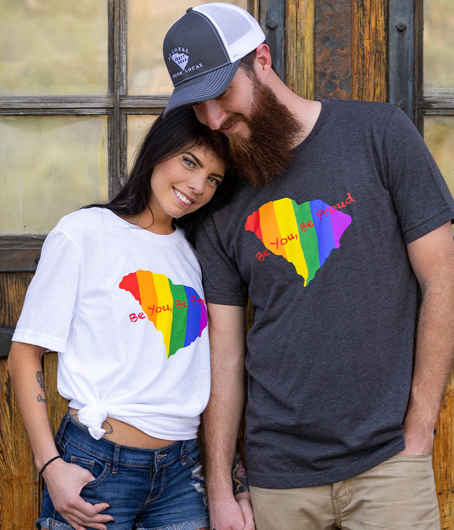 Male model in grey T-Shirt and Female model in white T-shirt, both with the rainbow state of SC with the words Be You, Be Proud in red written across the top of it.