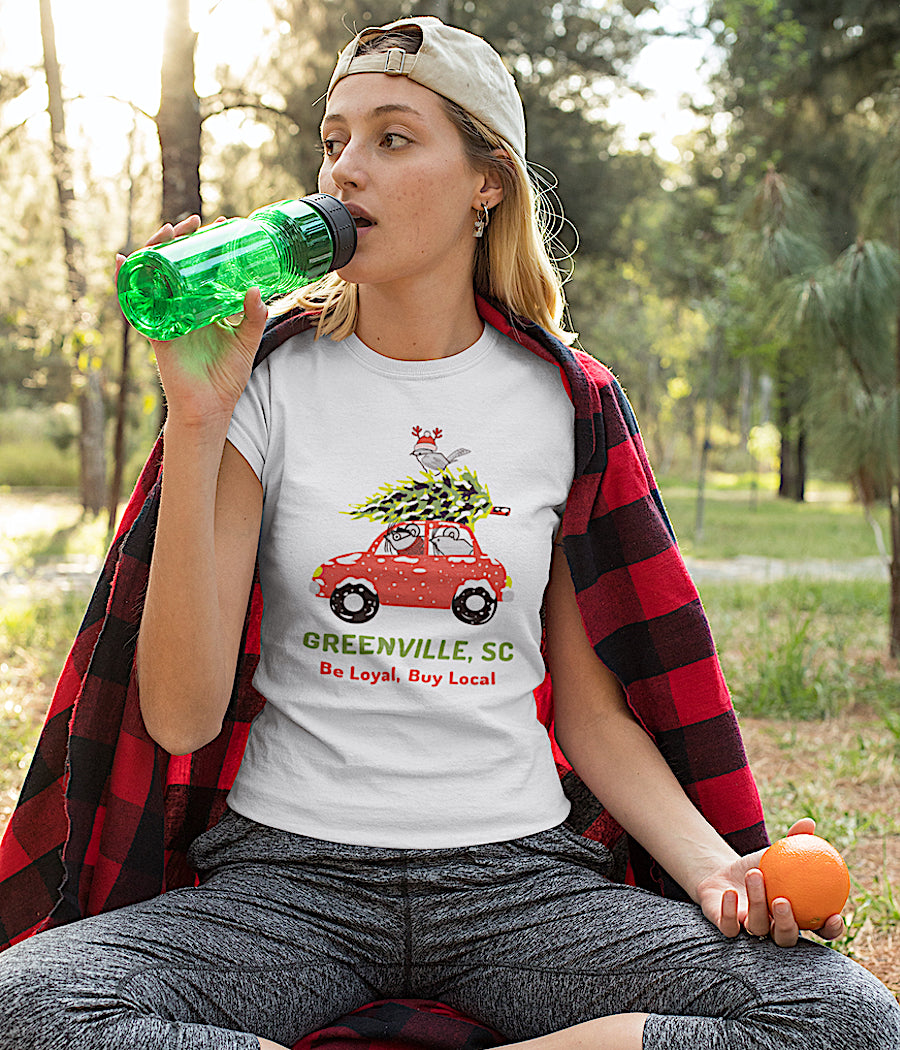 Girl siting in field in the White Greenville Women's Fall/Xmas Mouse Design short sleeve T-Shirt with local design of red car with 2 SC Mice in the car, a tree on top of the car and the state bird - the Carolina Wren is on top with a knit cap with reindeer antlers.